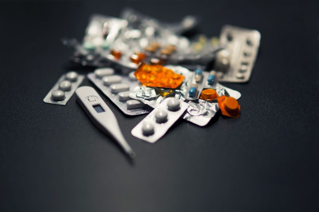 heros-img Close-up of various pills and a digital thermometer against a dark background.