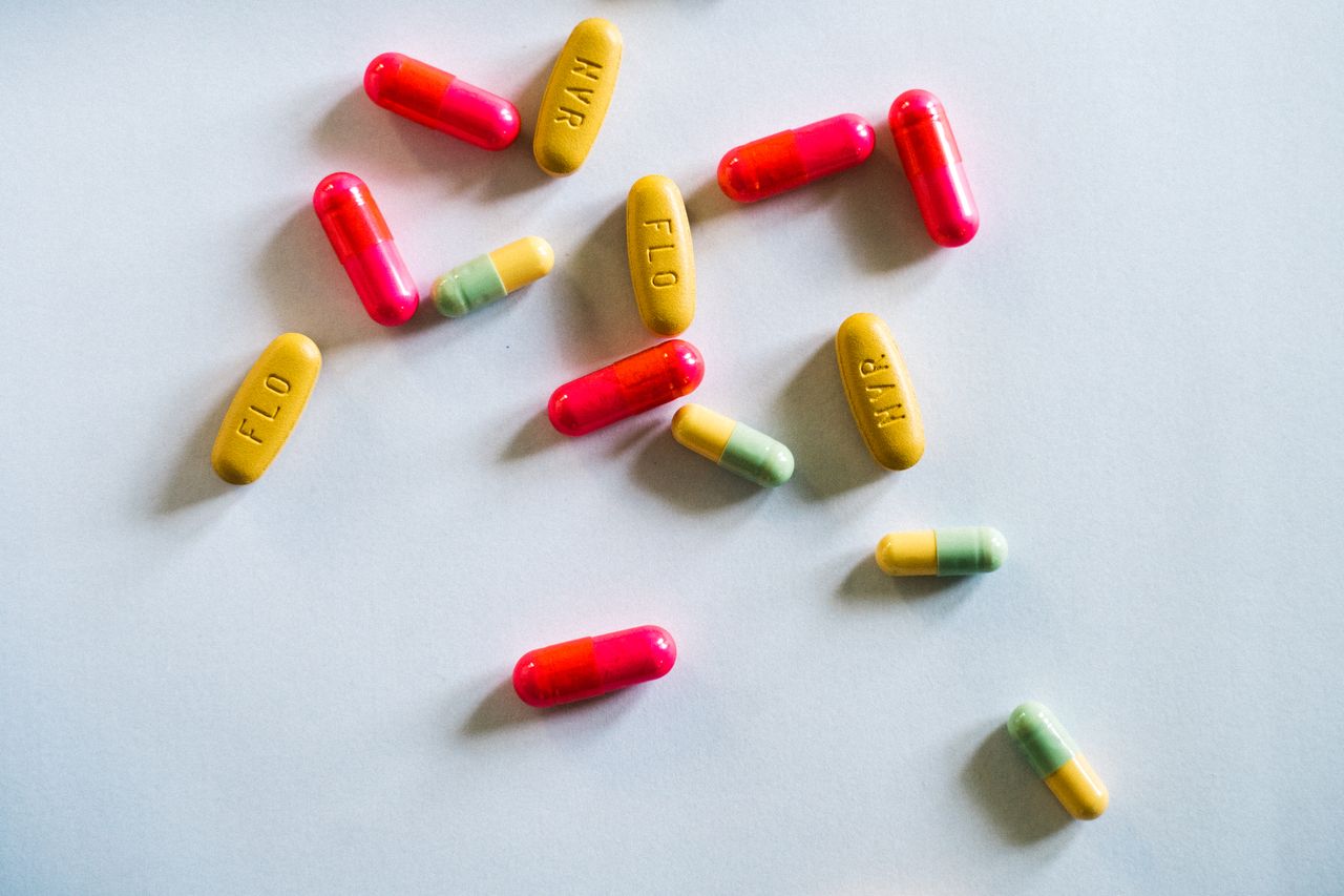 about-us-01 Various colorful pills scattered on a white surface, top view.