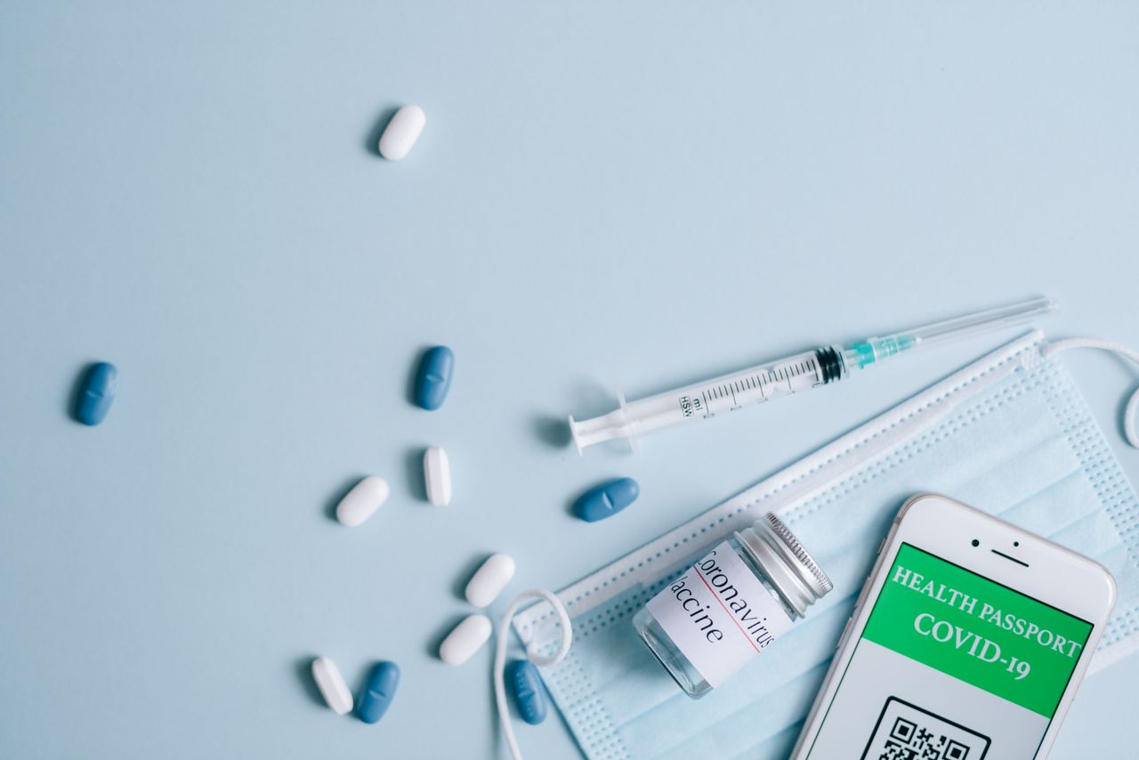 about-us-02 A flat lay of COVID-19 vaccination items including a mask, syringe, and health passport.